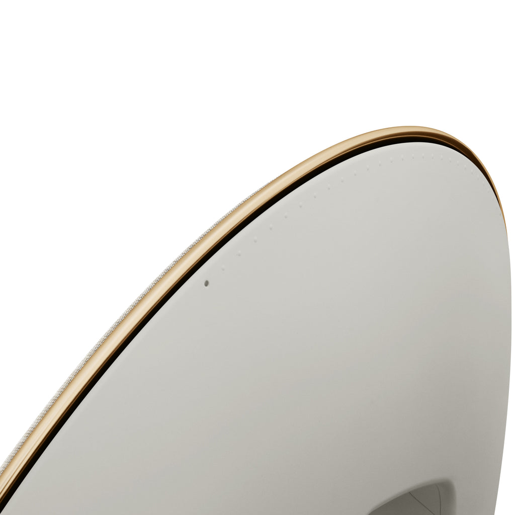 Makro-Aufnahme des oberen Randes der Beosound A9. Der goldfarbene Aluminiumring rahmt den Stoffbezug perfekt ein; dezente Touch-Indikatoren für die Lautstärke sind sichtbar.