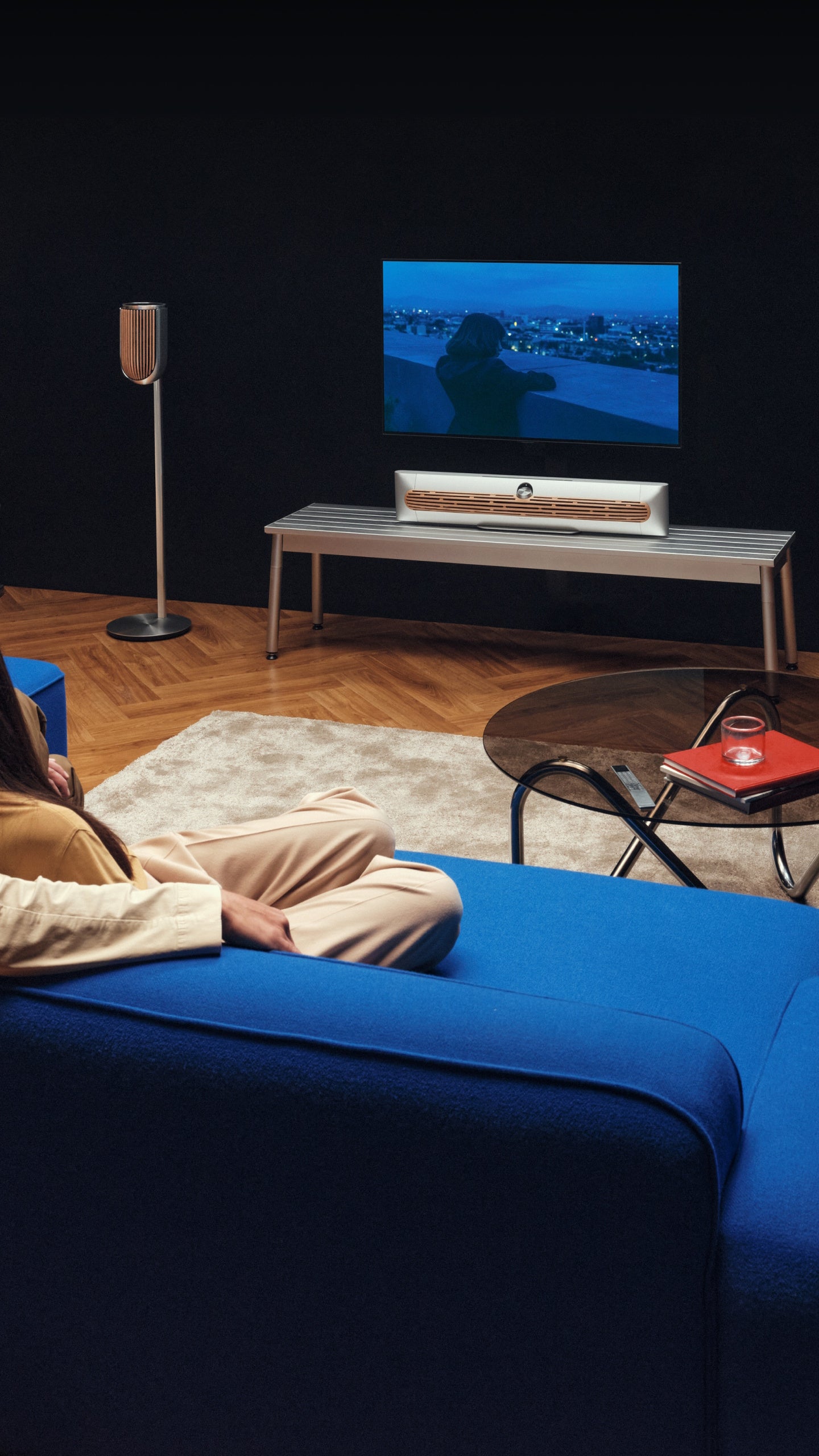 dunkles Wohnzimmer mit einem Fernseher an der Wand darunter die Beosound Premiere Soundbar in Silber mit cover aus Eichenholz
