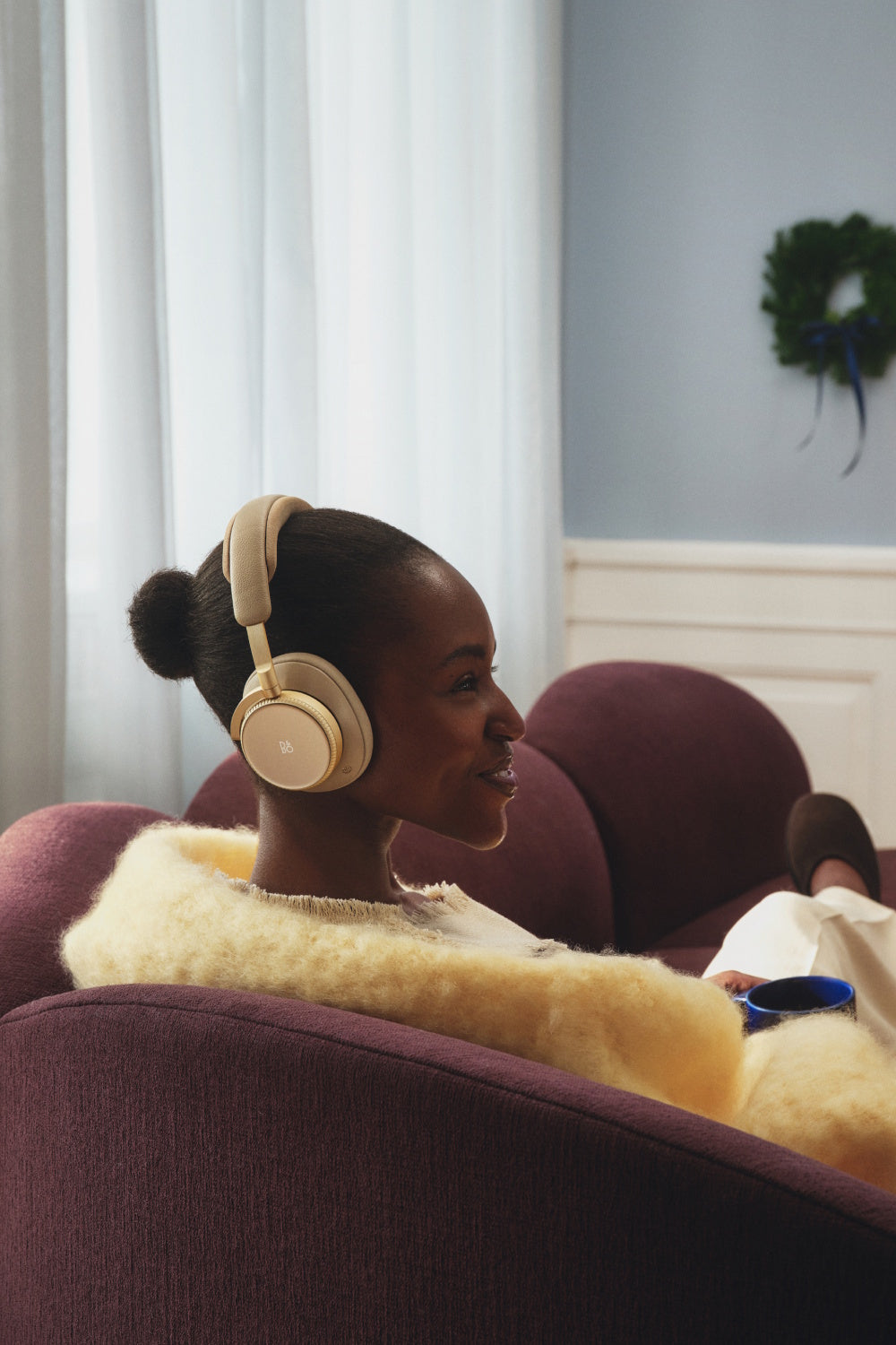 Frau sitzt auf der Couch und hat einen Beoplay h100 auf