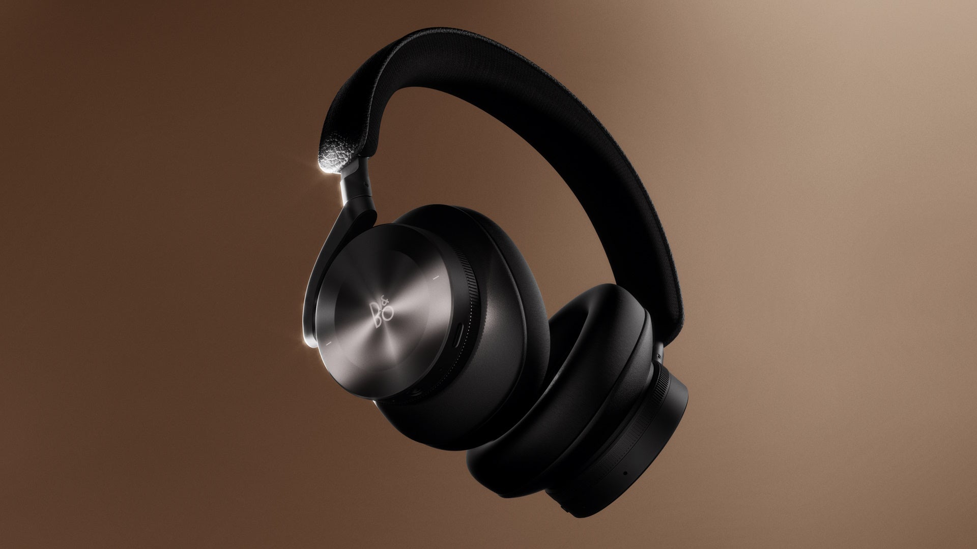 Freigestellte Produktaufnahme der Bang & Olufsen Beoplay H95 Over-Ear-Kopfhörer in Anthrazit-Schwarz, schwebend vor einem warmen braunen Farbverlaufshintergrund.