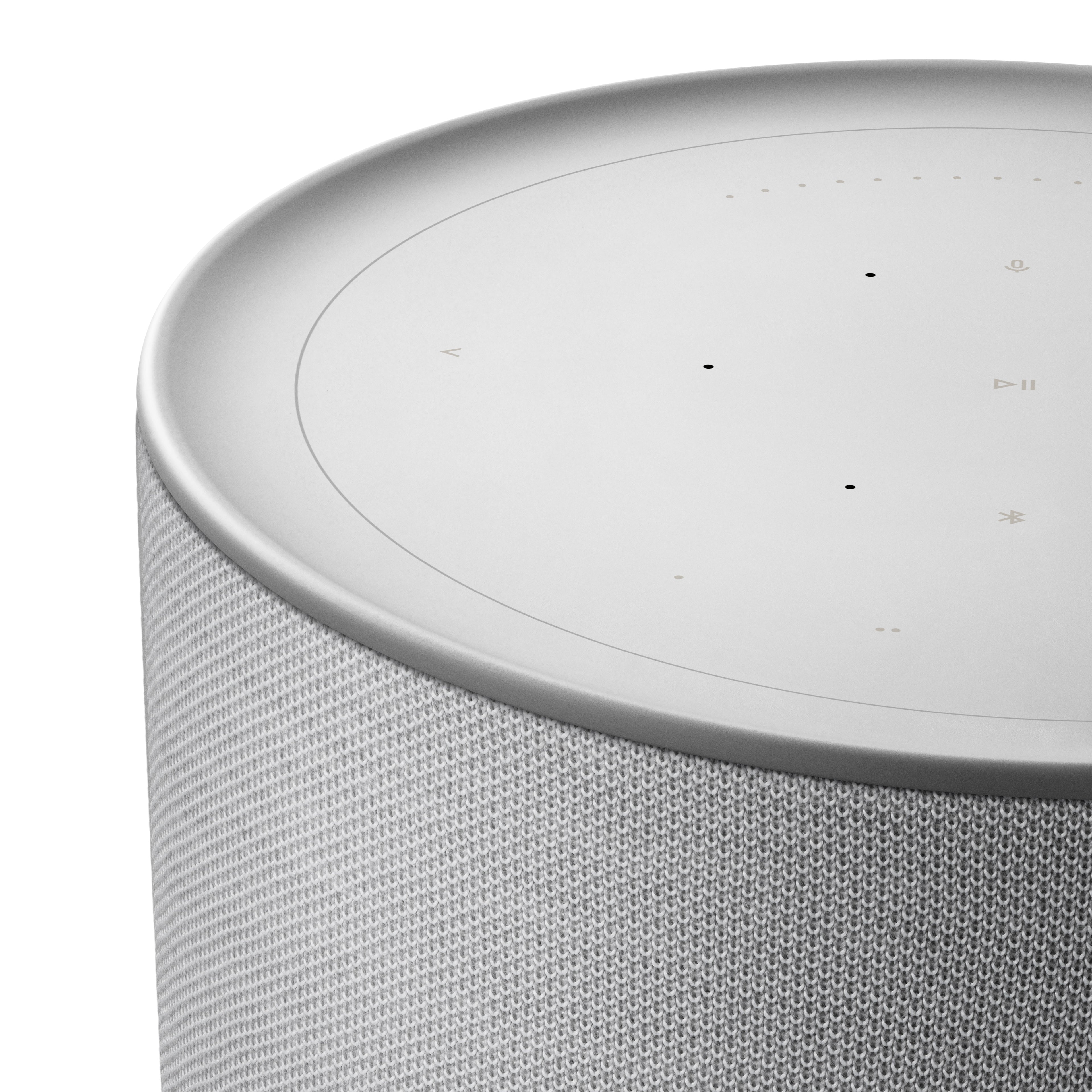 Detailaufnahme der Oberseite des Bang & Olufsen Beosound Balance in Natural Aluminium. Gezeigt wird die elegante Aluminium-Einfassung der Touch-Oberfläche und der Übergang zum fein gewebten, grauen Textilbezug bei hellem Studiolicht.